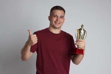 Happy winner with golden trophy cup showing thumbs up on light grey background