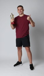 Photo of Happy winner with golden trophy cup showing thumbs up on light grey background