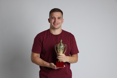 Photo of Happy winner with golden trophy cup on light grey background