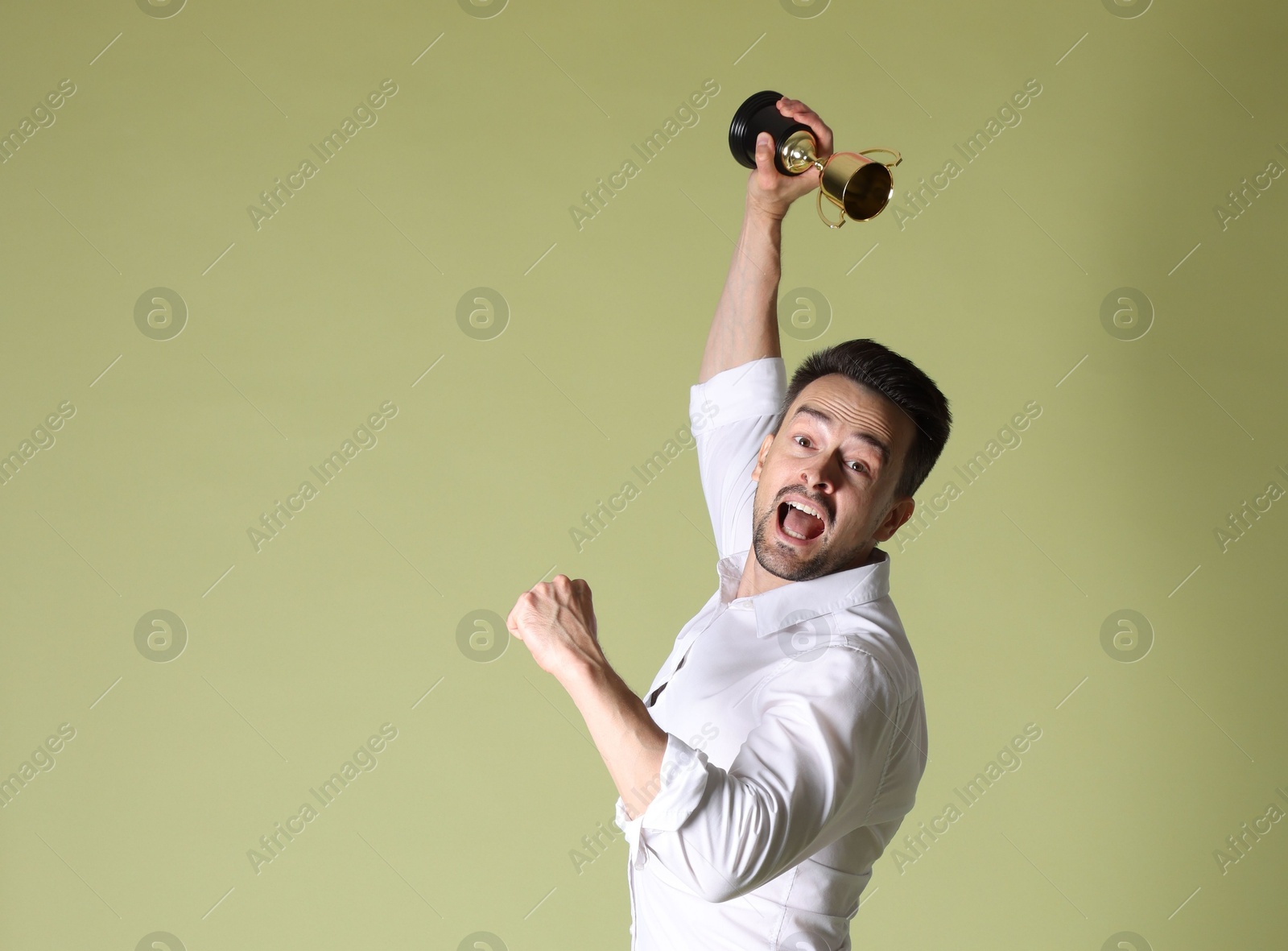 Photo of Happy winner with golden trophy cup on pale olive background, space for text