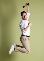 Photo of Happy winner with golden trophy cup jumping on pale olive background