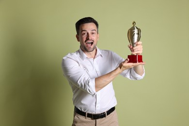 Photo of Happy winner with golden trophy cup on pale olive background