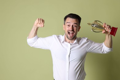 Photo of Happy winner with golden trophy cup on pale olive background