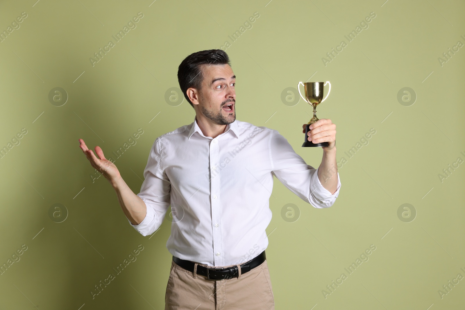 Photo of Surprised winner with golden trophy cup on pale olive background