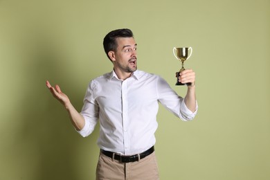 Surprised winner with golden trophy cup on pale olive background