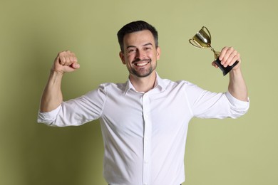 Photo of Happy winner with golden trophy cup on pale olive background