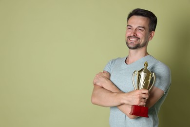 Happy winner with golden trophy cup on pale olive background, space for text