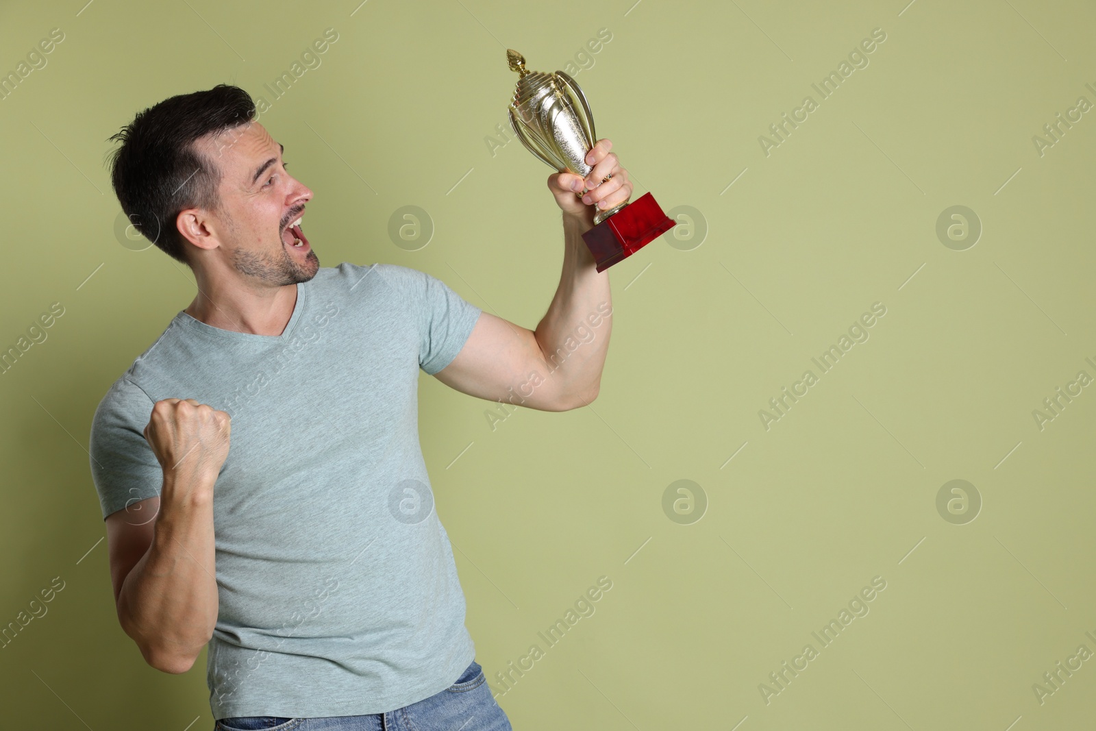 Photo of Happy winner with golden trophy cup on pale olive background, space for text