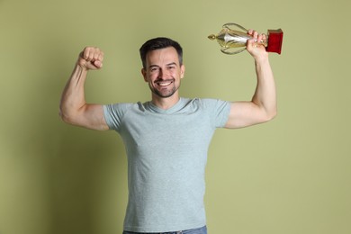 Photo of Happy winner with golden trophy cup showing his biceps on pale olive background