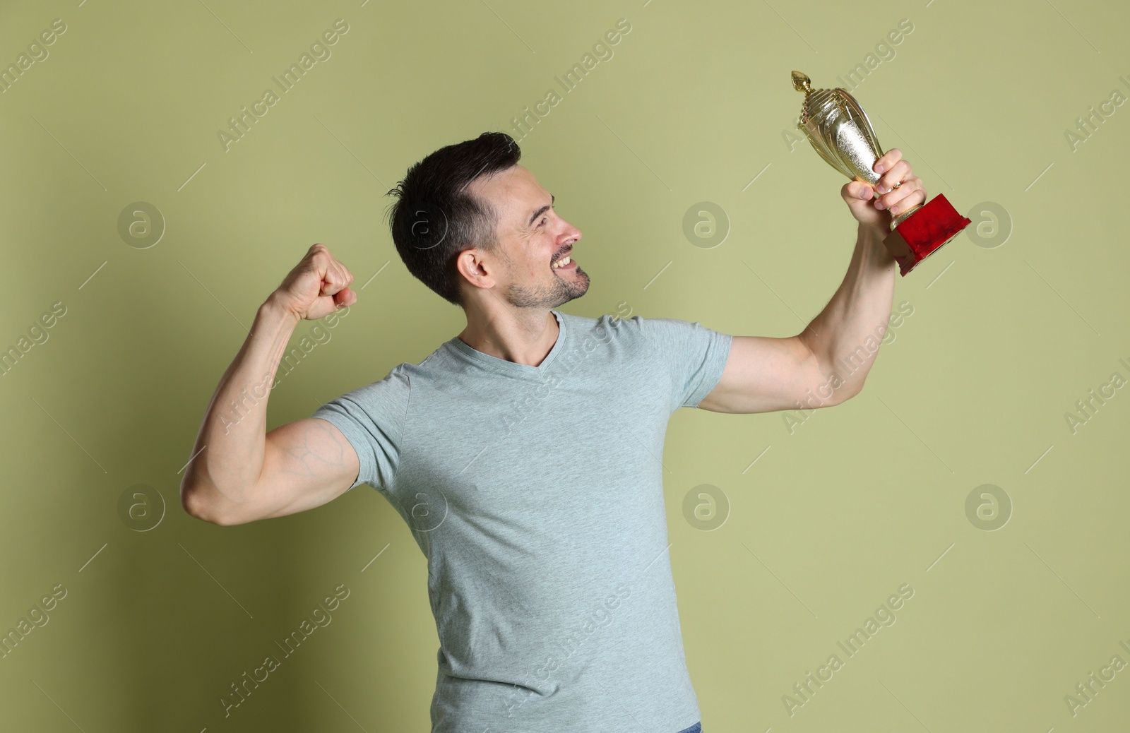 Photo of Happy winner with golden trophy cup on pale olive background