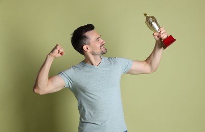 Happy winner with golden trophy cup on pale olive background