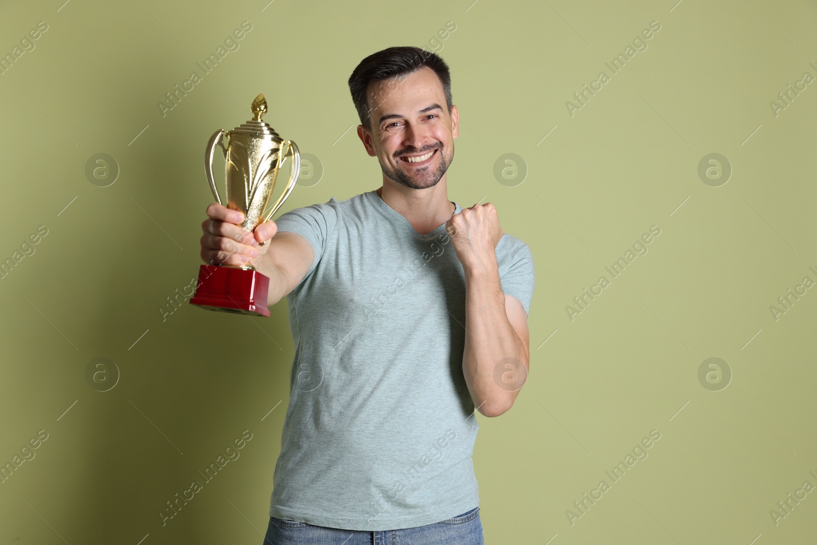 Photo of Happy winner with golden trophy cup on pale olive background