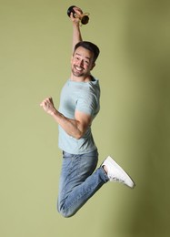 Photo of Happy winner with golden trophy cup jumping on pale olive background