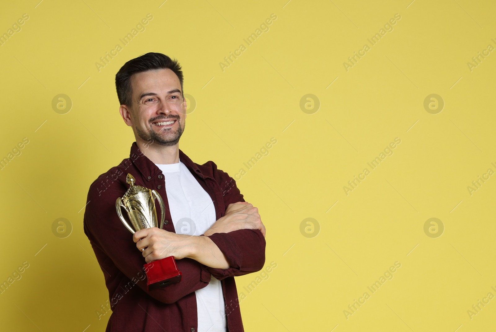 Photo of Happy winner with golden trophy cup on yellow background, space for text