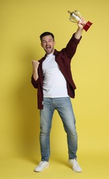 Photo of Happy winner with golden trophy cup on yellow background