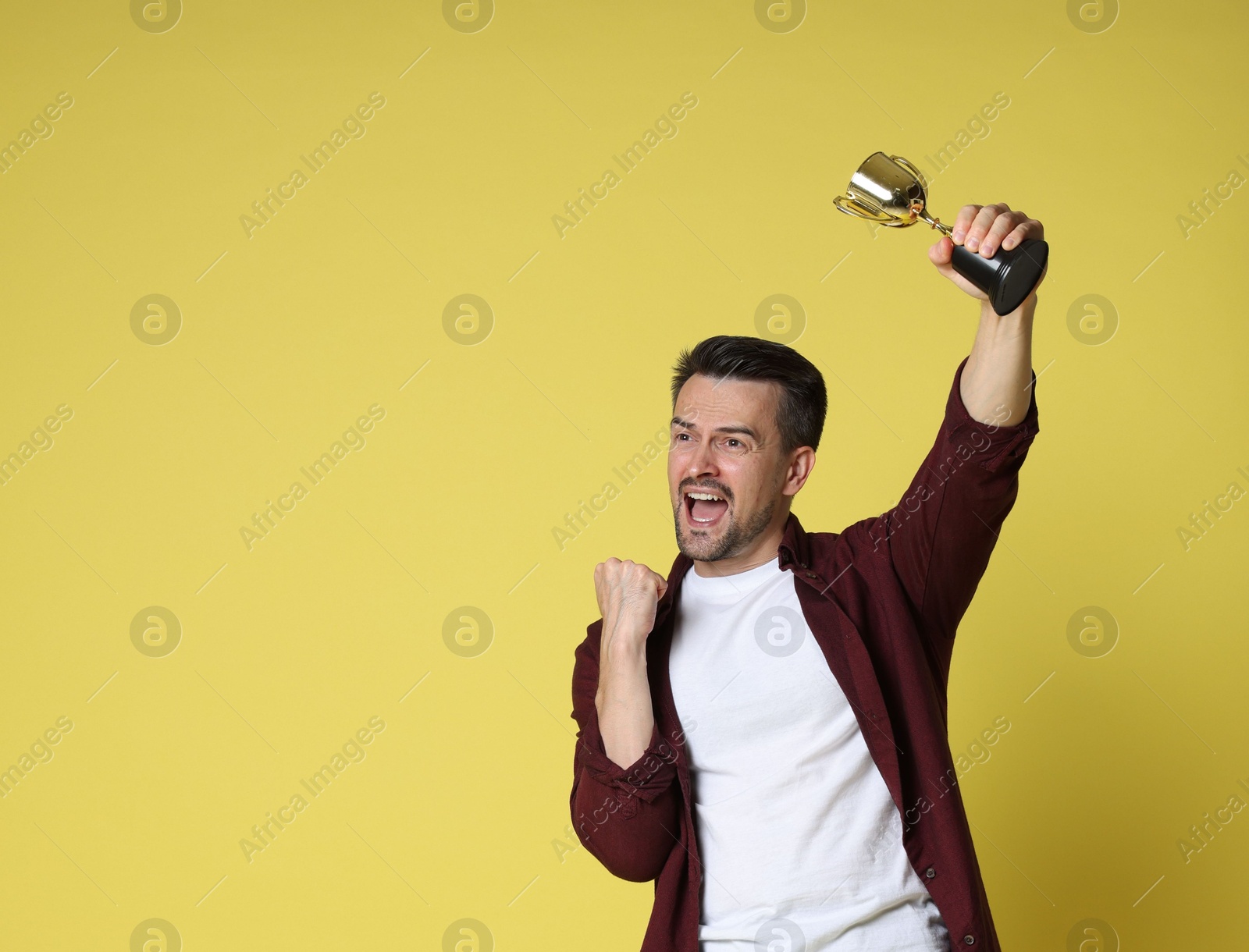 Photo of Happy winner with golden trophy cup on yellow background, space for text