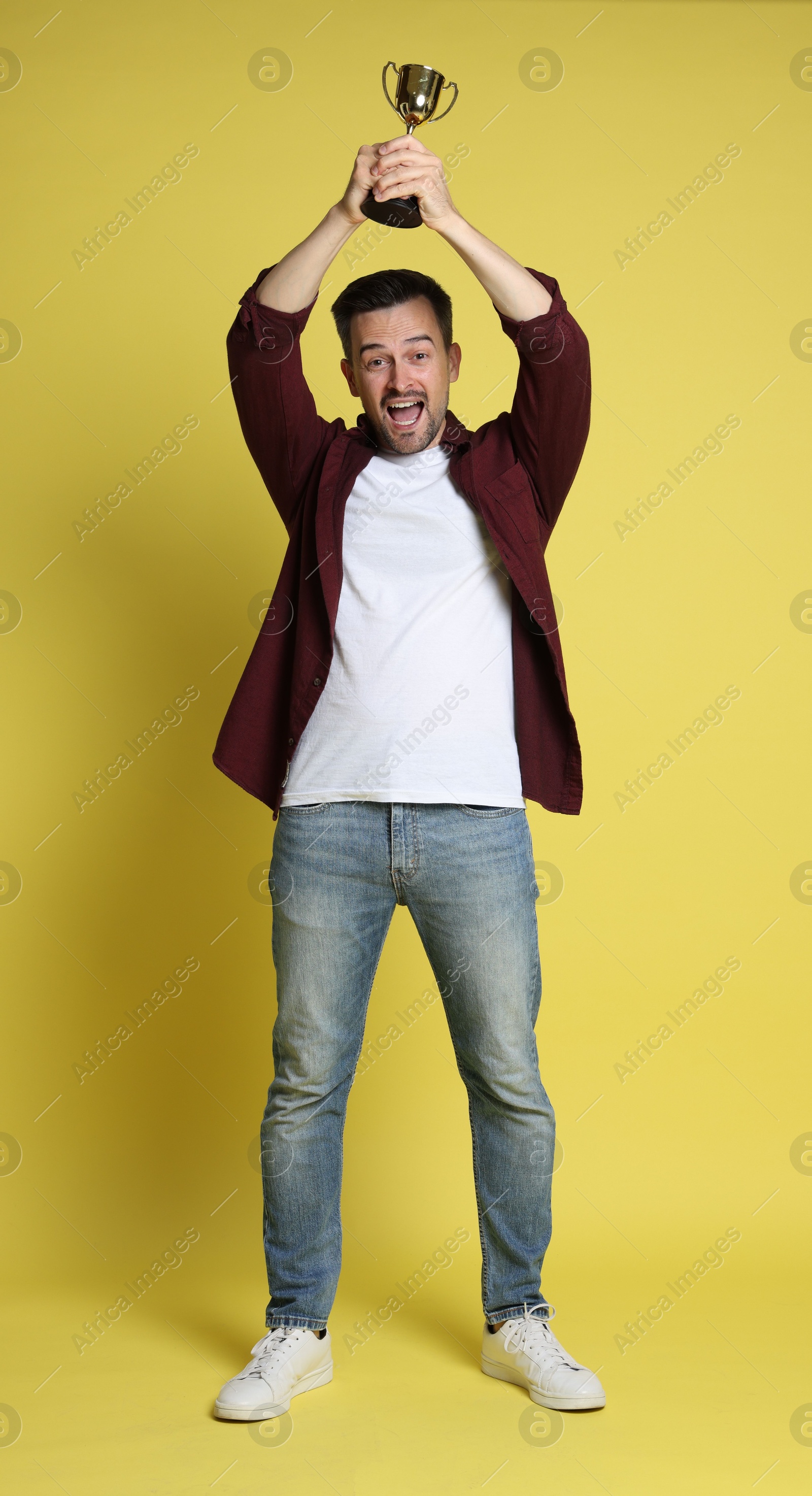 Photo of Happy winner with golden trophy cup on yellow background