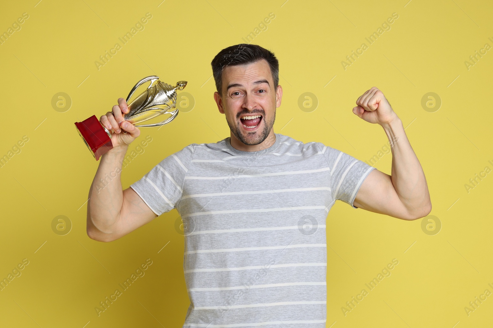 Photo of Happy winner with golden trophy cup on yellow background