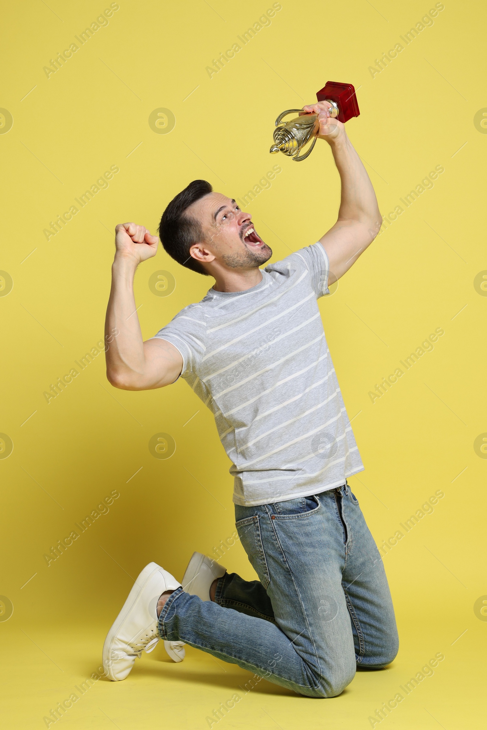 Photo of Happy winner with golden trophy cup on yellow background