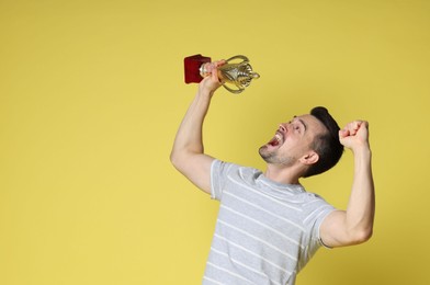 Happy winner with golden trophy cup on yellow background, space for text