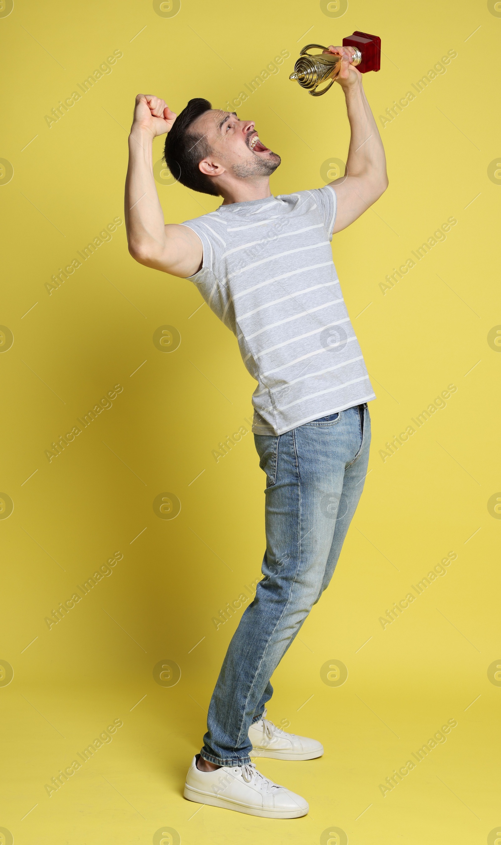 Photo of Happy winner with golden trophy cup on yellow background