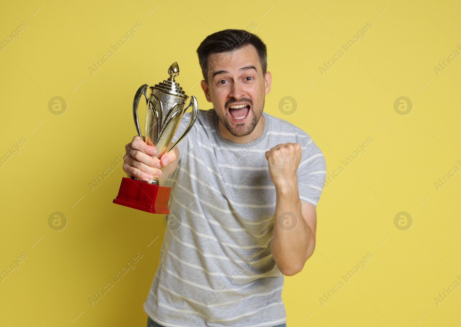 Photo of Happy winner with golden trophy cup on yellow background