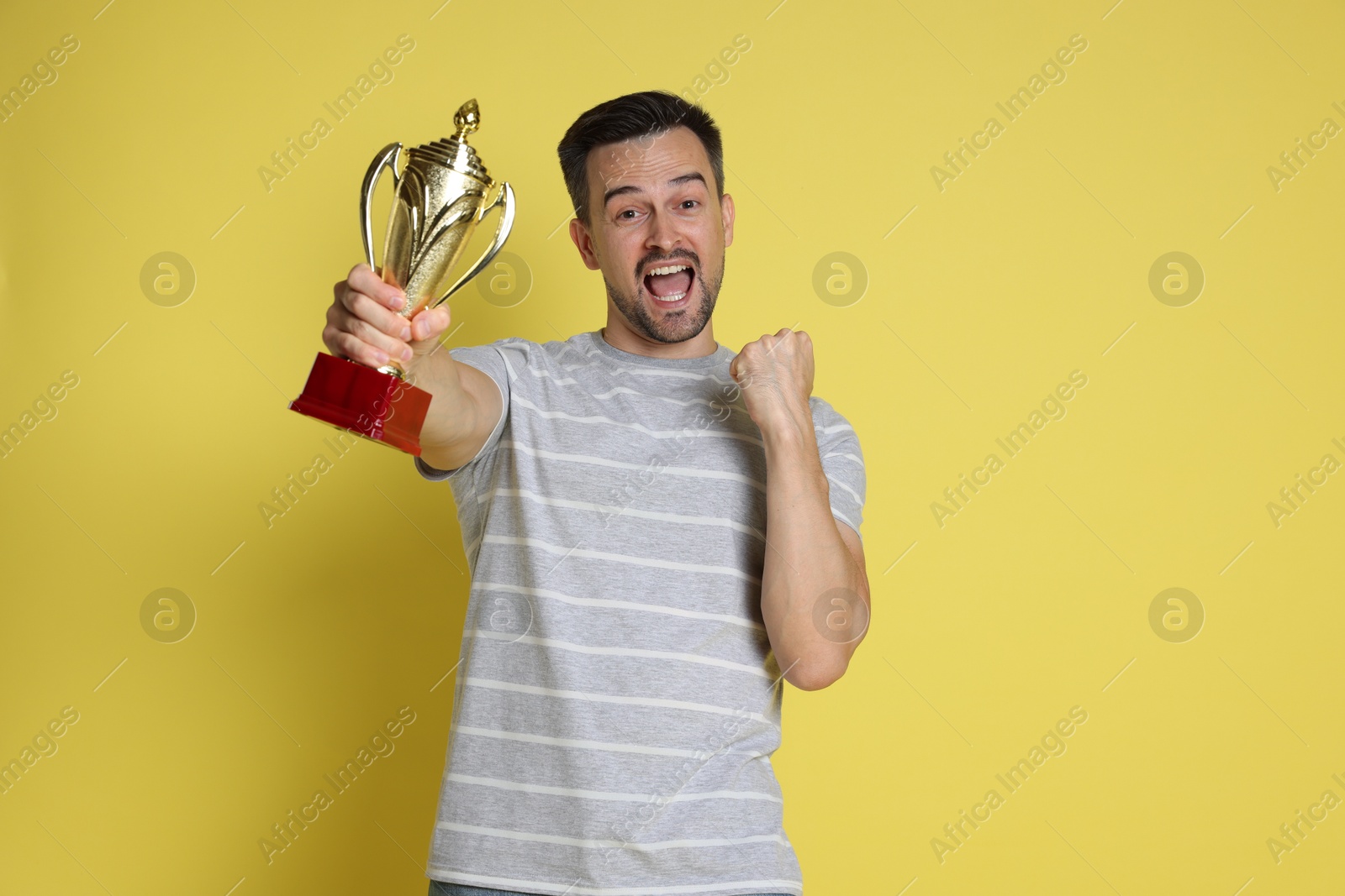 Photo of Happy winner with golden trophy cup on yellow background