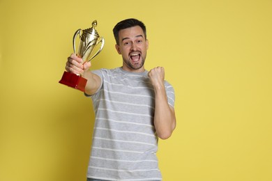 Photo of Happy winner with golden trophy cup on yellow background