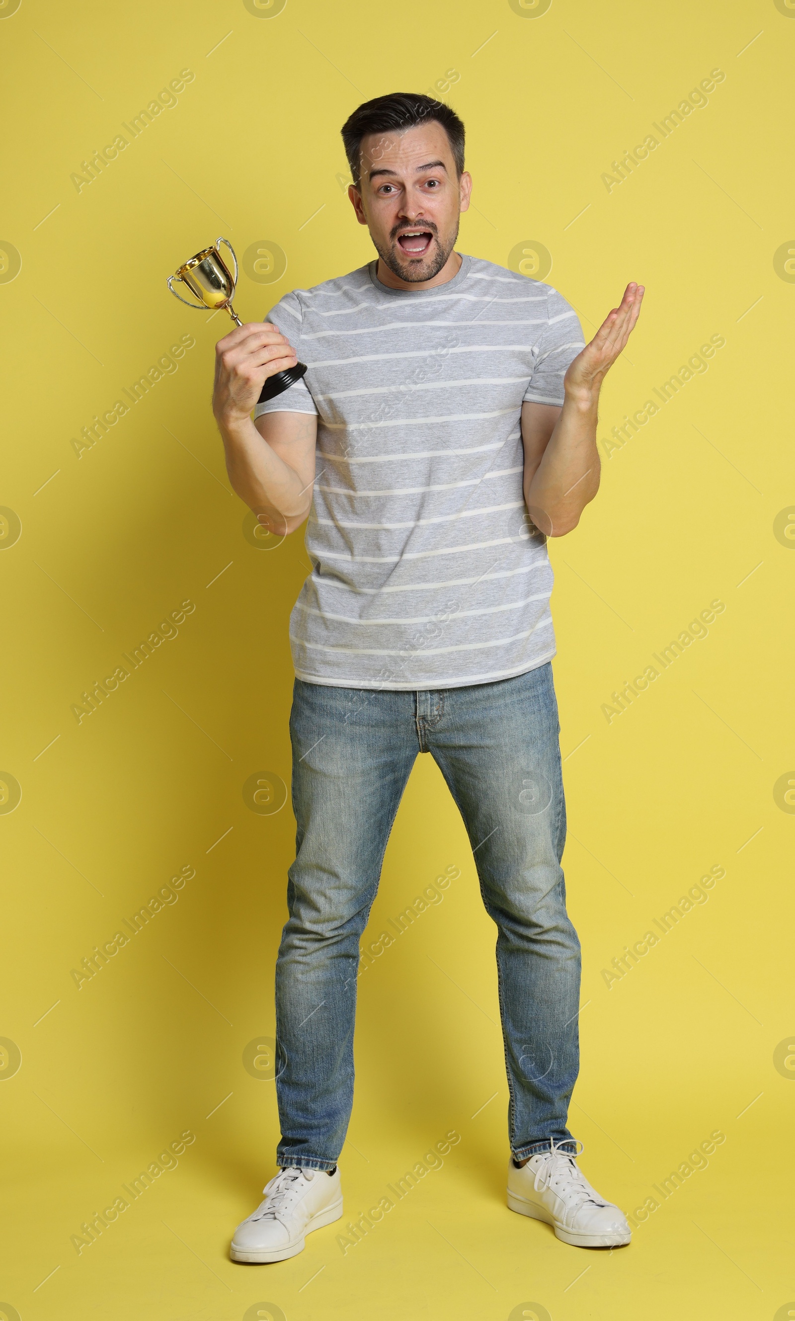 Photo of Emotional winner with golden trophy cup on yellow background