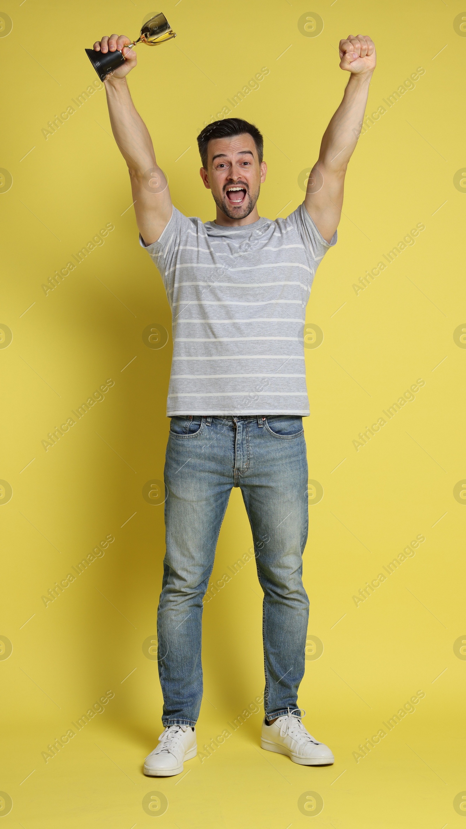 Photo of Happy winner with golden trophy cup on yellow background