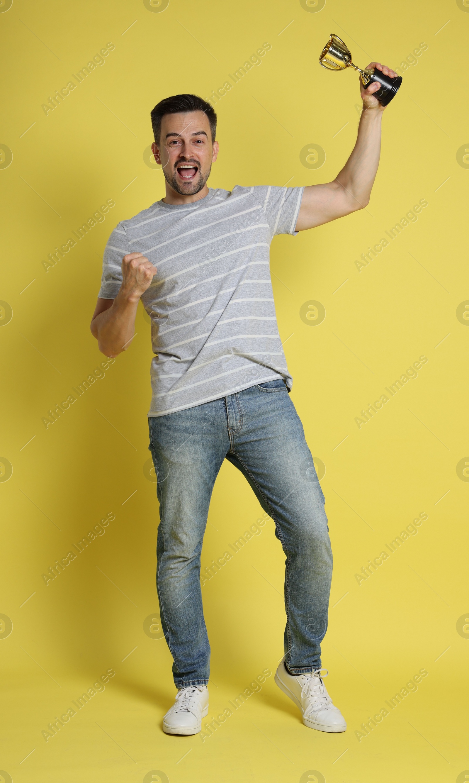 Photo of Happy winner with golden trophy cup on yellow background