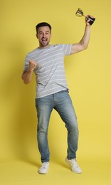 Photo of Happy winner with golden trophy cup on yellow background