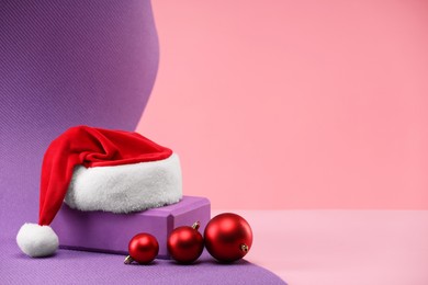 Photo of Yoga mat, Santa hat and baubles on pink background, space for text