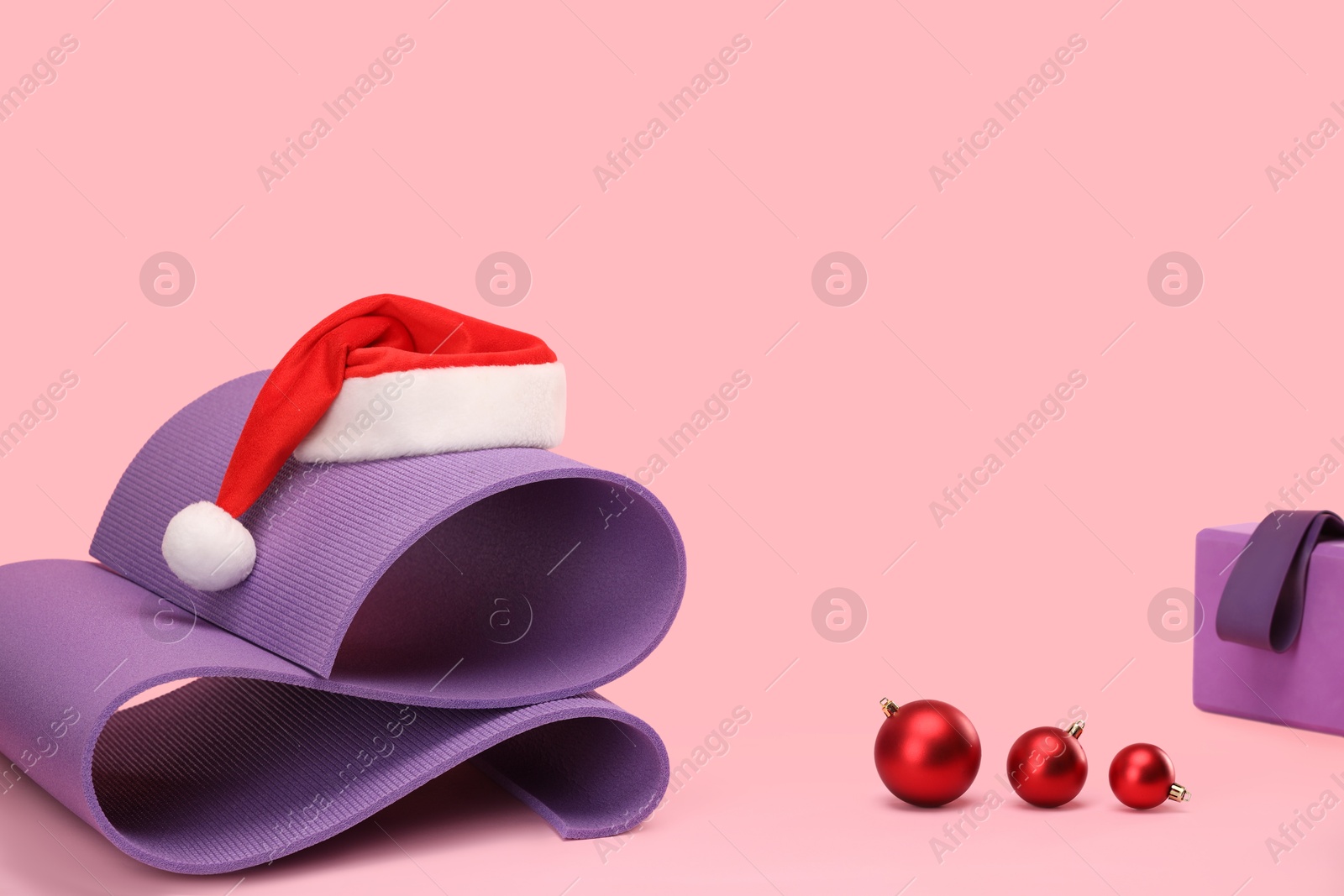 Photo of Yoga mat, block, Santa hat and baubles on pink background