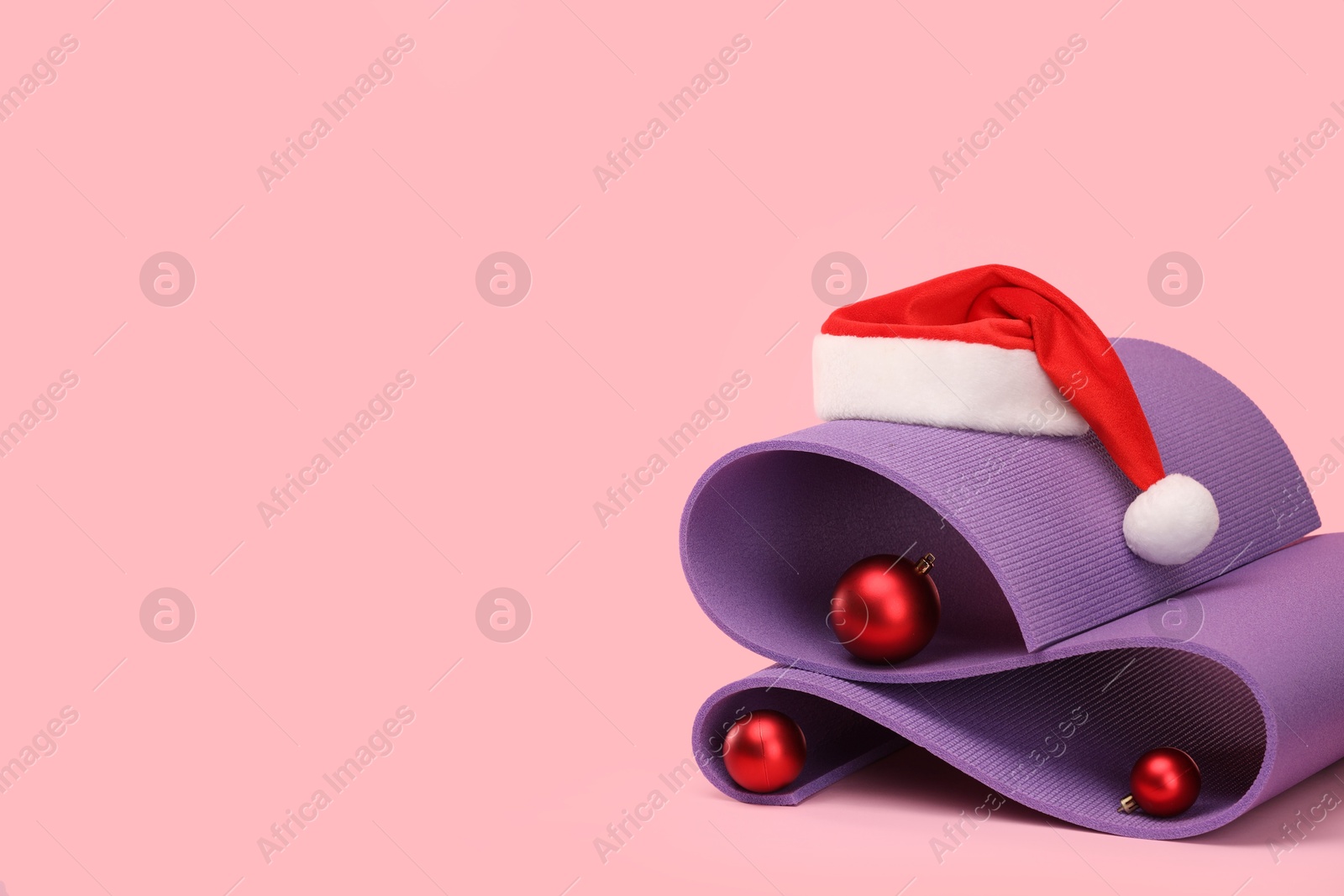 Photo of Yoga mat, Santa hat and baubles on pink background, space for text