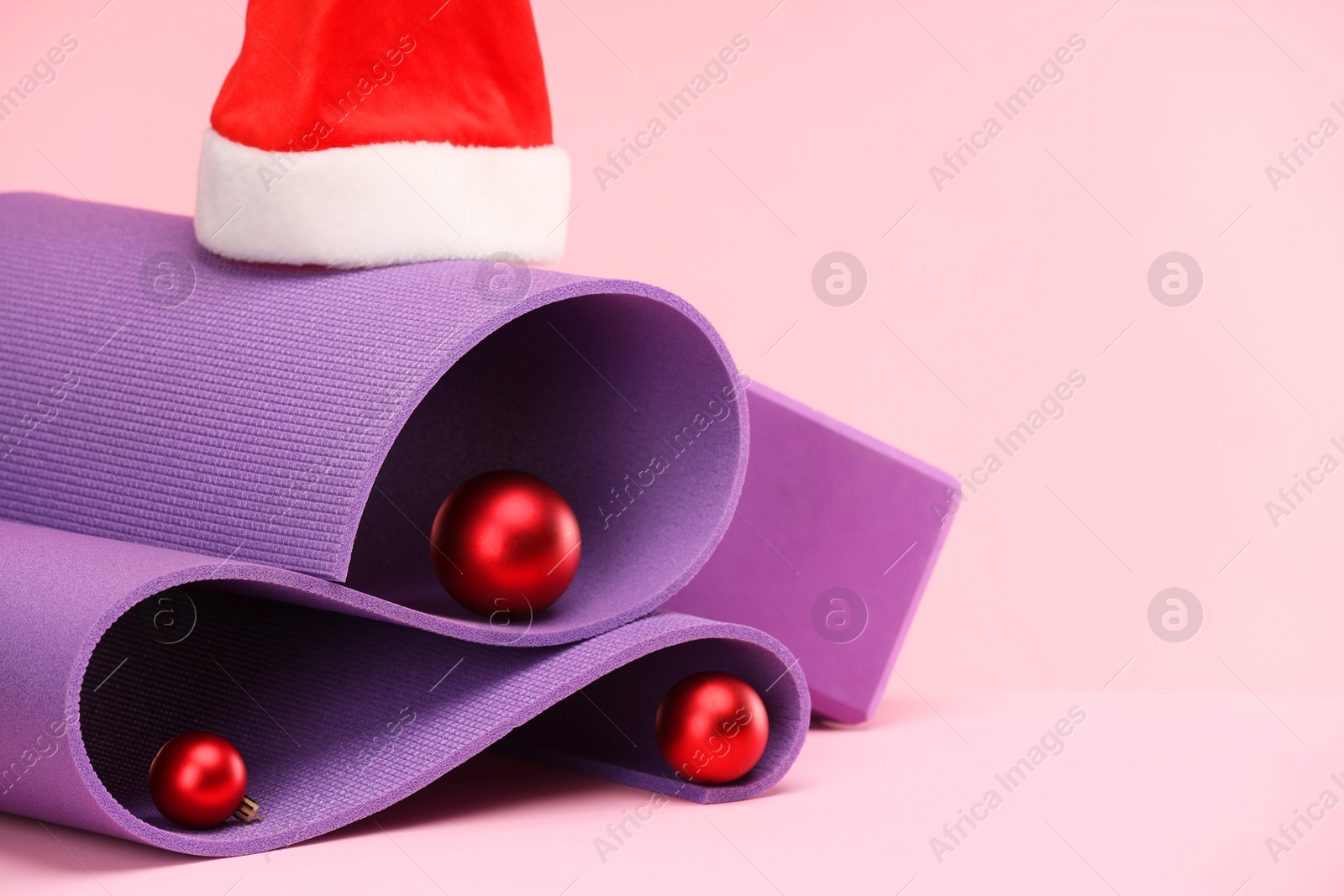 Photo of Yoga mat, Santa hat and baubles on pink background, space for text