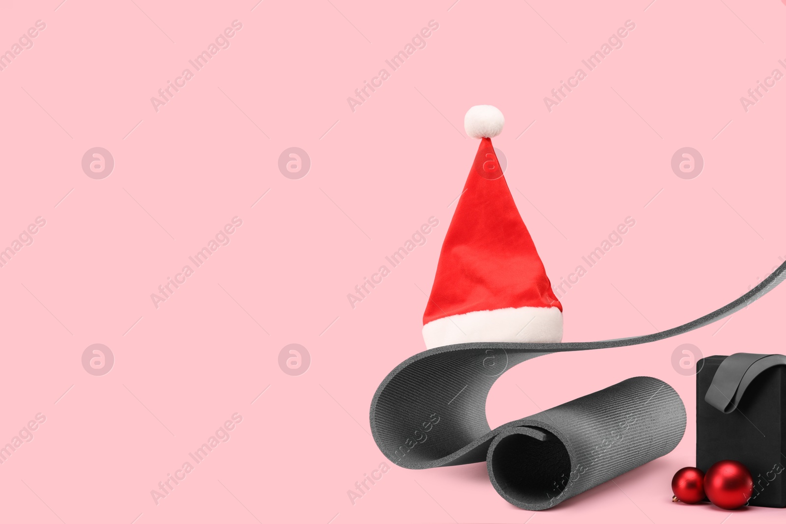 Photo of Yoga mat, block, Santa hat and baubles on pink background, space for text