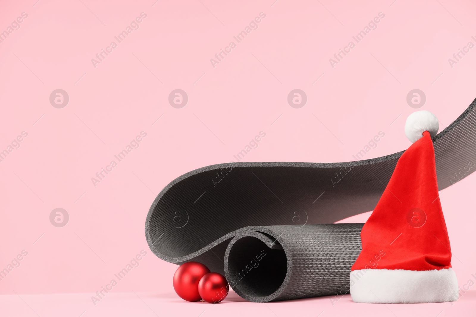 Photo of Yoga mat, Santa hat and baubles on pink background, space for text