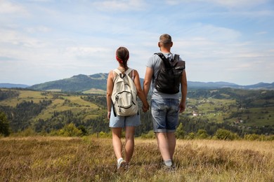 Photo of Couple with backpacks walking to mountains, back view. Active tourism