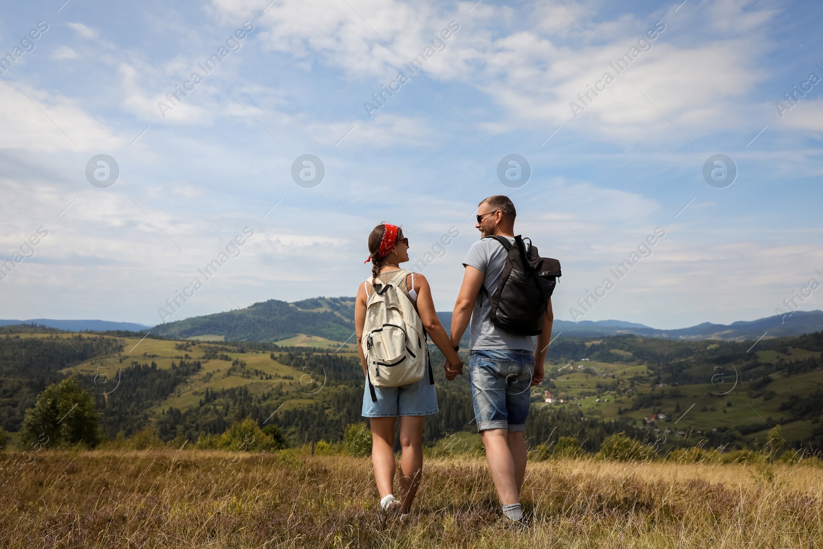 Photo of Couple with backpacks walking to mountains, back view. Active tourism