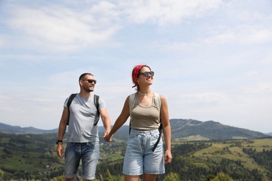 Happy couple with backpacks walking in mountains, space for text. Active tourism