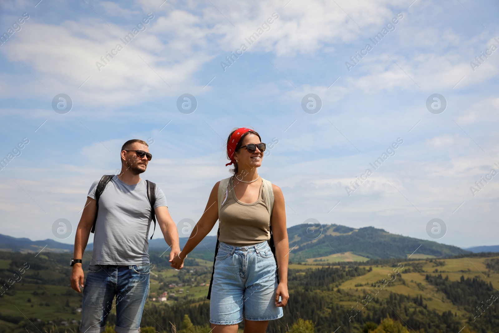 Photo of Happy couple with backpacks walking in mountains, space for text. Active tourism