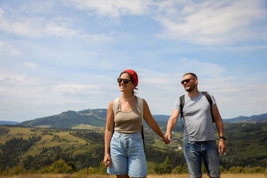 Photo of Happy couple with backpacks walking in mountains, space for text. Active tourism