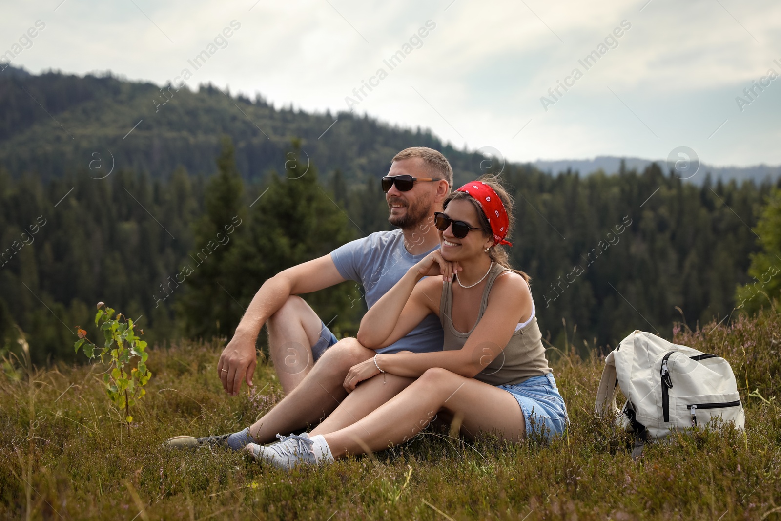 Photo of Happy couple with backpack resting on grass outdoors. Active tourism