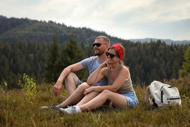 Happy couple with backpack resting on grass outdoors. Active tourism