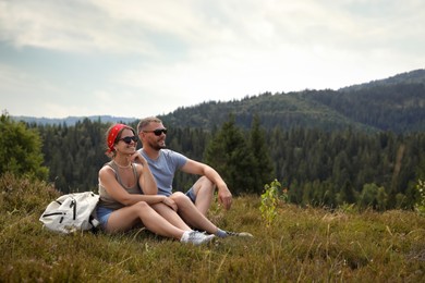 Happy couple with backpack resting on grass outdoors, space for text. Active tourism