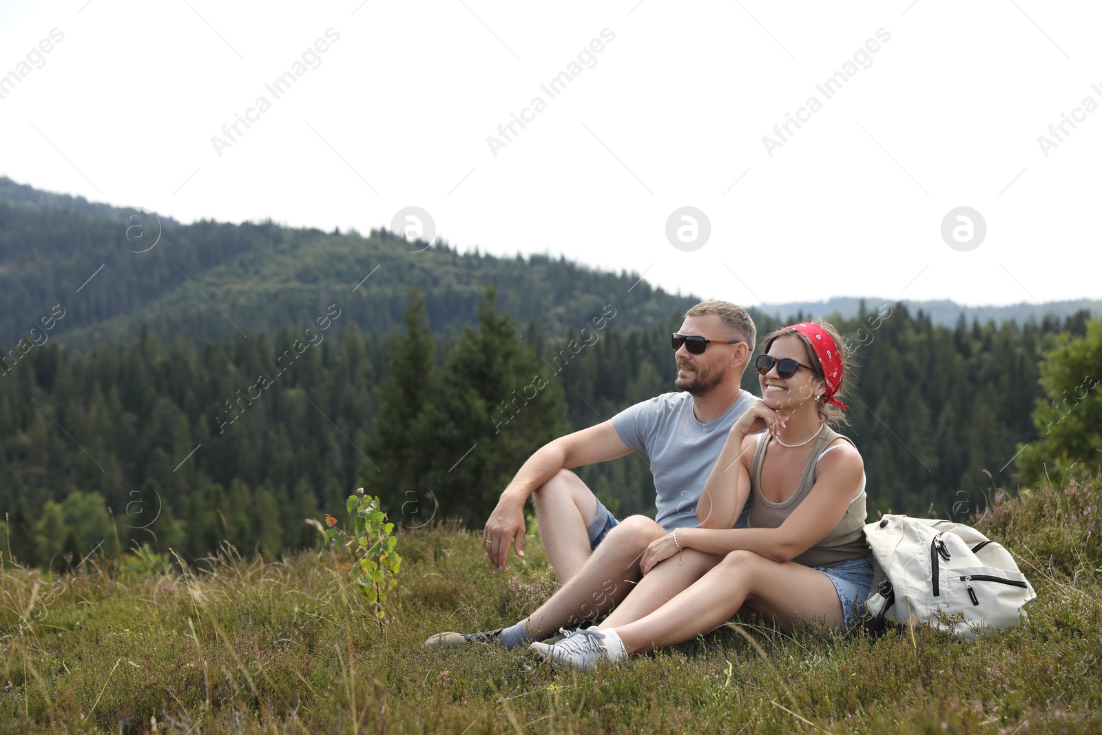 Photo of Happy couple with backpack resting on grass outdoors, space for text. Active tourism