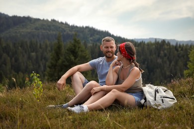 Photo of Happy couple with backpack resting on grass outdoors. Active tourism