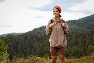 Smiling tourist with backpack walking in mountains. Space for text