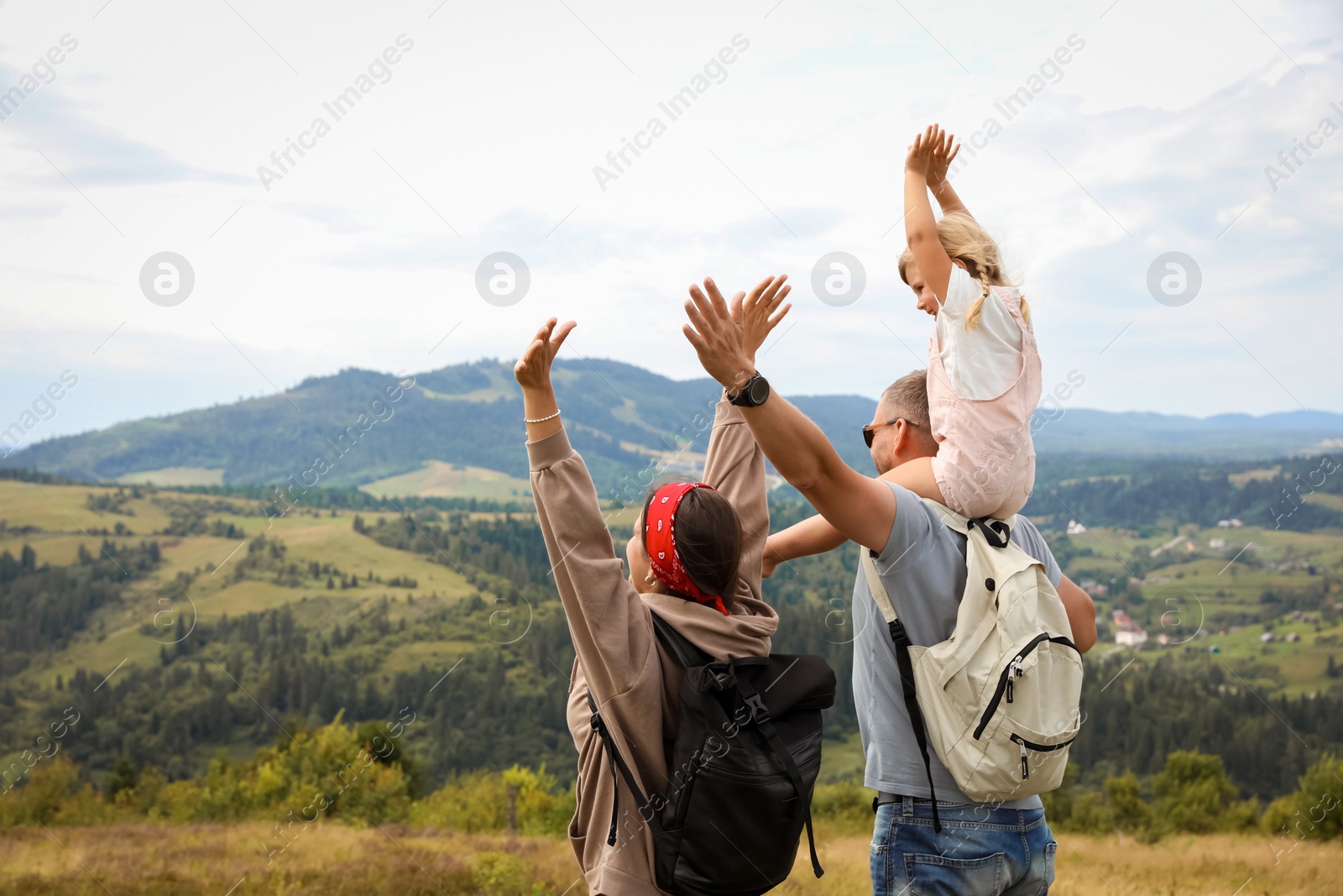 Photo of Family of tourists with backpacks enjoying picturesque landscape with wide open arms, back view. Space for text